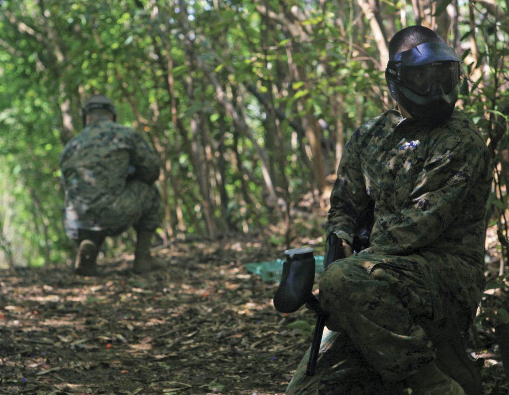 Paintball players in masks taking cover in the woods